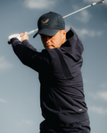 Golfer in midnight navy performance hoodie swinging a golf club against a blue sky