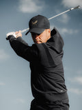 Golfer wearing black Golf Pinnacle Performance Hoodie mid swing against a blue sky
