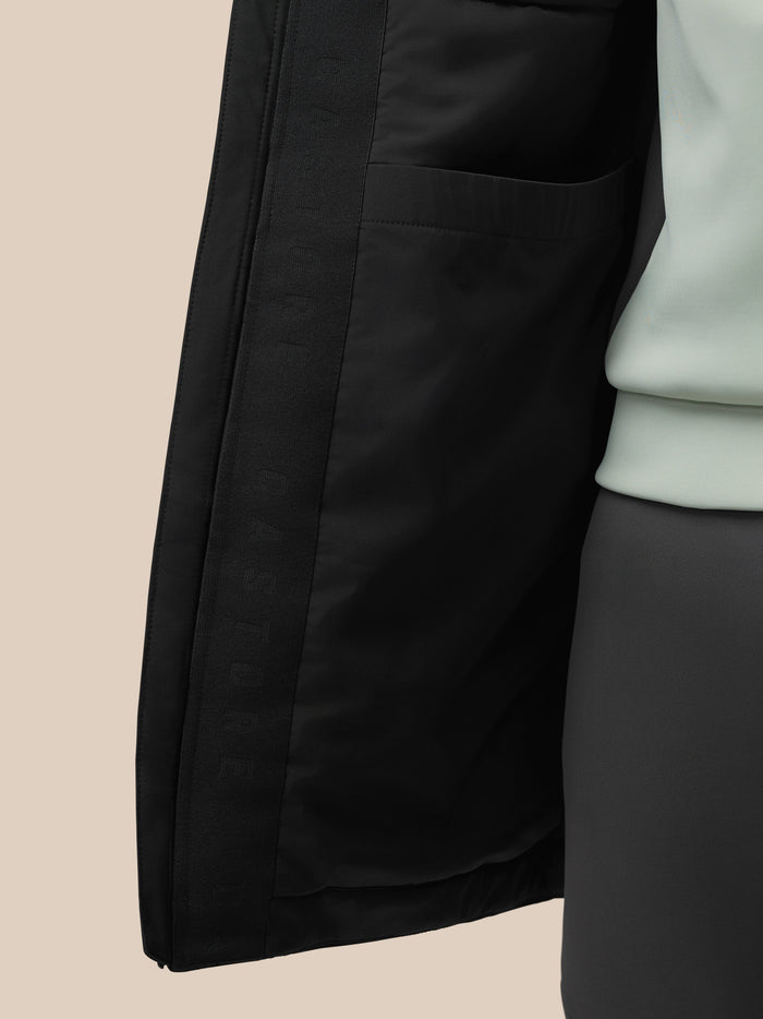 Close-up of the black longline wadded jacket showing a front pocket seam and stitched edge detail