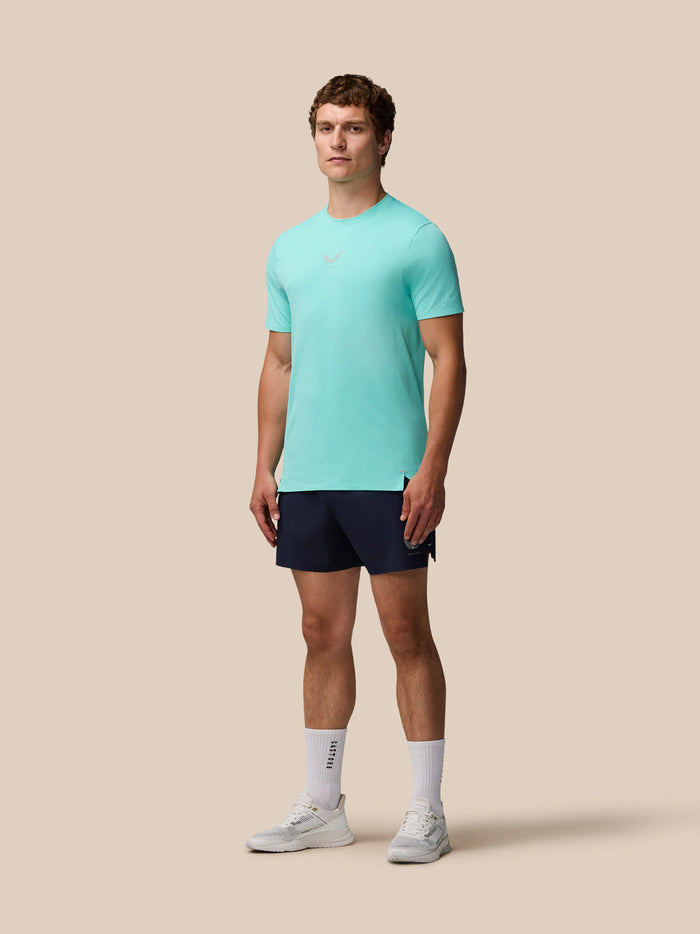 Male model wearing Zone Training T-Shirt in light aqua with navy shorts against a beige backdrop