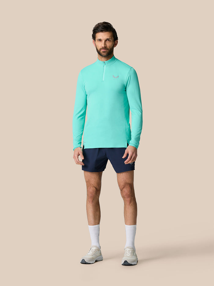 Full body shot of a man wearing a light aqua Zone Training 1/4 Zip Top with navy shorts.