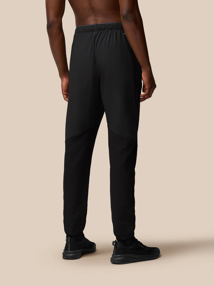 Back view of male model wearing black Flex Winterised Woven Joggers with a jacket showing textured lower legs