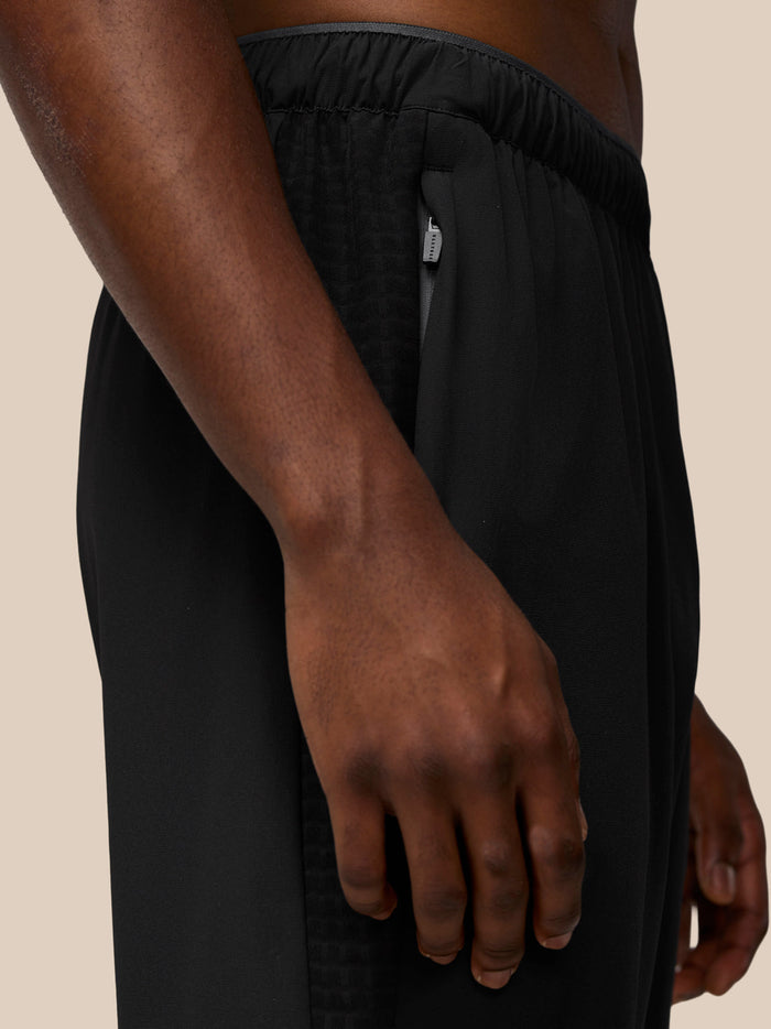 Side view of black joggers featuring a hip zip pocket and subtle paneling.