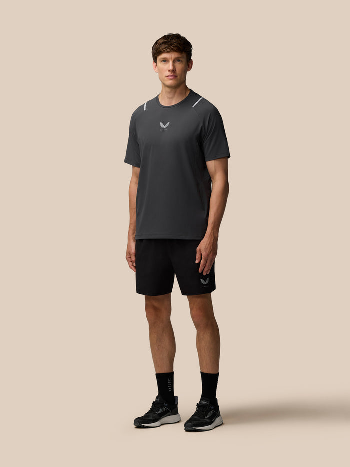 Male model wearing a dark Castore athletic T shirt with chest logo against a beige background