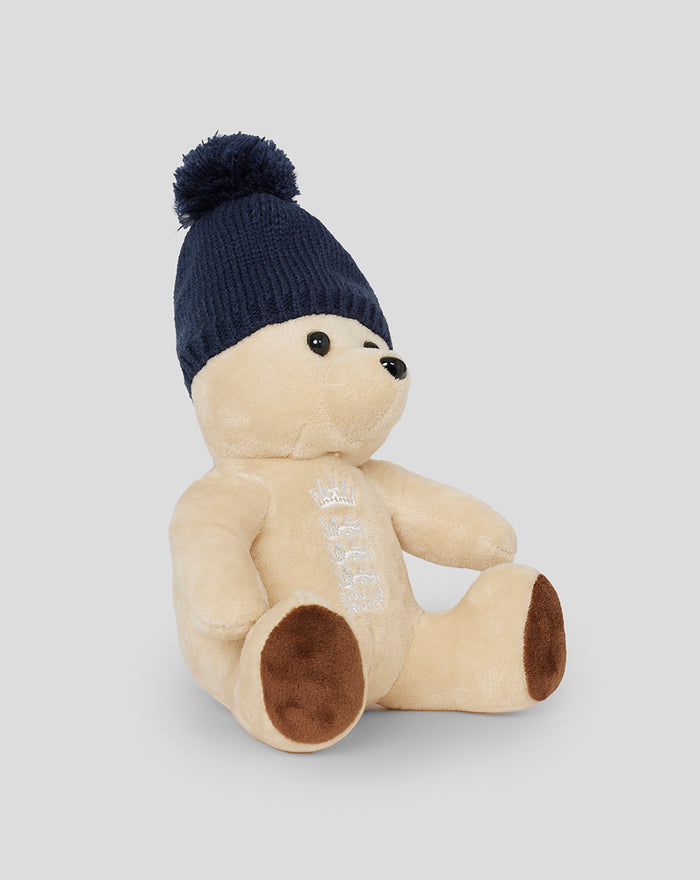 Side view of England cricket bear plush in cream fur wearing a navy knit beanie