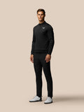 Male model wearing black Golf Club Trousers with white golf shoes against a beige backdrop