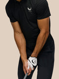 Man wearing black Castore Golf Pinnacle Pique Stripe Polo with subtle stripes and chest logo while gripping a golf club.