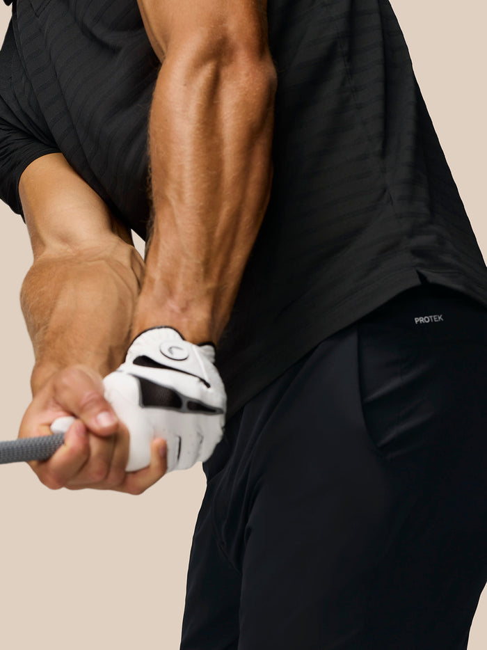 Rear three-quarter view of a man in a black striped golf polo showing Castore branding on the upper back.