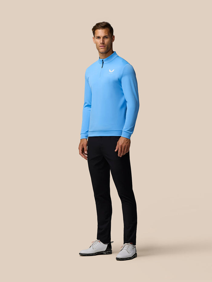 Full-body view of a man wearing the Golf Club Classic Quarter Zip Top in cool blue with center front zip and Castore logo