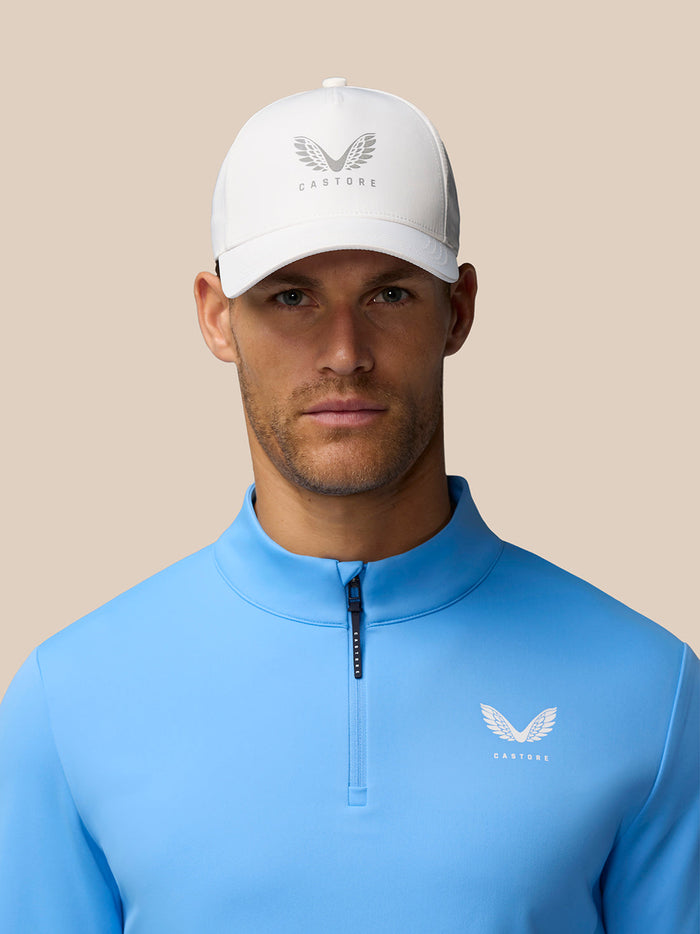 Front view of man wearing blue Club Classic quarter zip top and white cap with Castore logo on chest