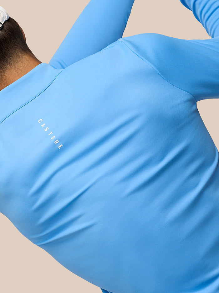 Back view of person wearing Cool Blue Club Classic quarter zip top with Castore logo on left chest and white cap