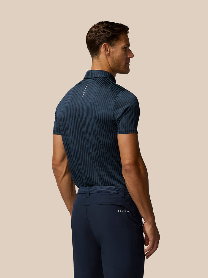 Back view of a male model wearing a midnight navy striped Golf Pinnacle Glow Polo with vertical Castore branding along the back