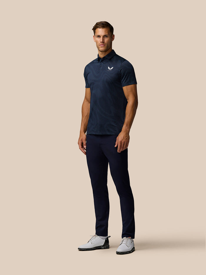 Full body shot of a male model in the navy striped Golf Pinnacle Glow Polo paired with navy trousers and white golf shoes