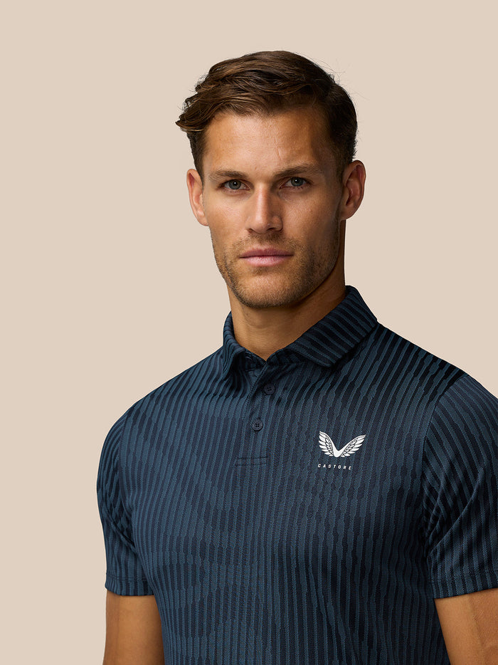 Close up of model wearing Golf Pinnacle Glow Polo in Midnight Navy showing all over stripes and left chest logo.