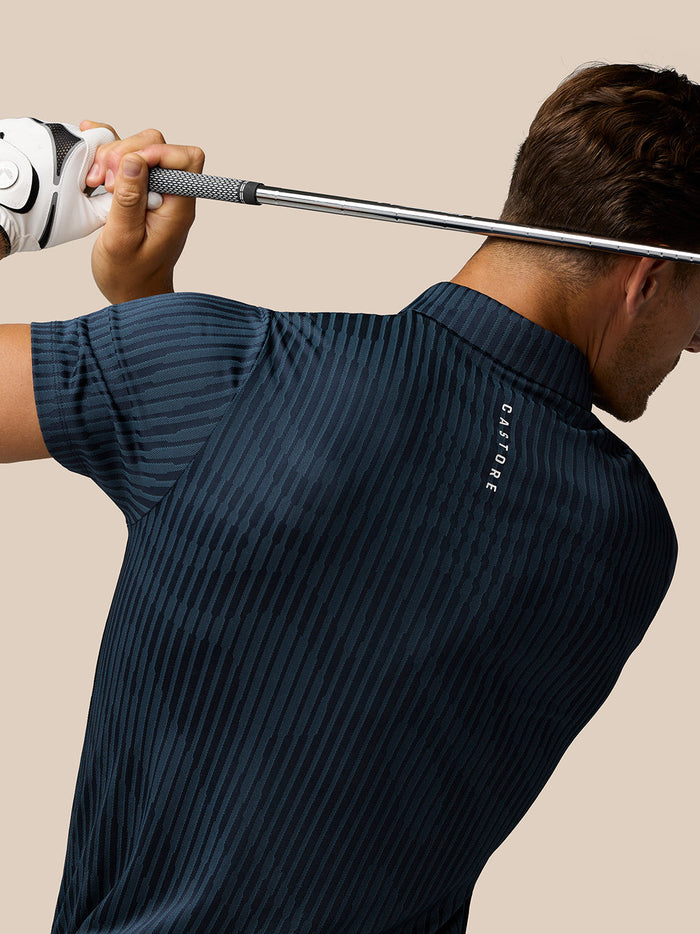 Back view of golfer wearing Midnight Navy Pinnacle Glow Polo with Castore branding along the back and a golf club held across the shoulders.