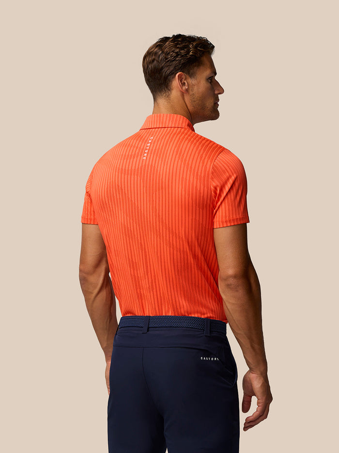 Back view of a man wearing a bright orange striped golf polo with Castore branding along the upper back