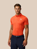 Male model wearing Golf Pinnacle Glow Polo in Bright Orange with striped knit and Castore logo on left chest.