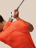 Rear view of a golfer wearing a bright orange striped Pinnacle Glow Polo while gripping a golf club
