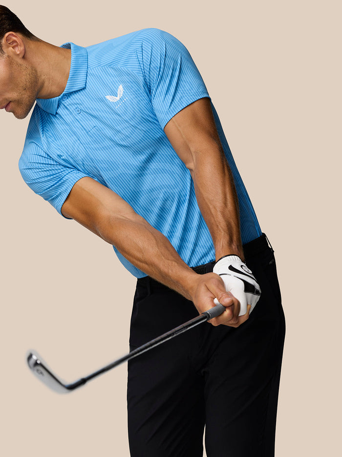 Golfer in a light blue Golf Club Glow Printed Polo mid swing with black pants and golf club in hand