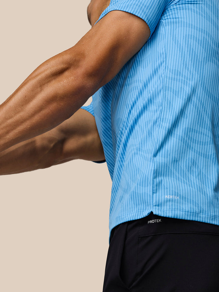 Side view of a man in a light blue Golf Club Glow Printed Polo showing the printed pattern and AerTek fabric near the hem