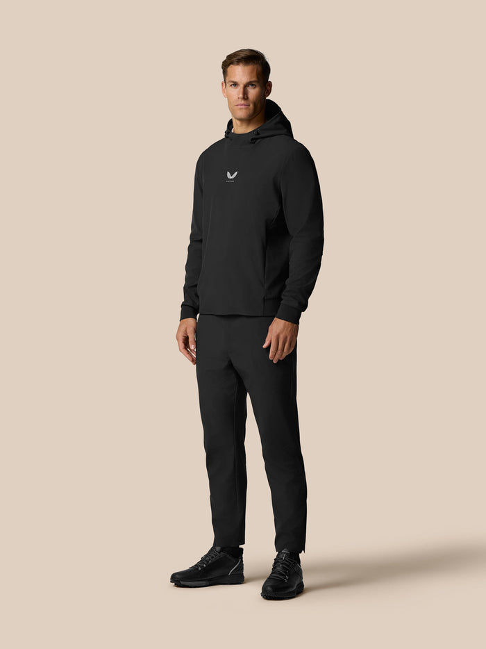 Full-length shot of a male model in black Golf Pinnacle Performance Hoodie with matching pants against a beige backdrop.