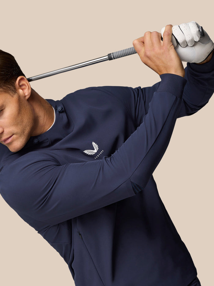 Male golfer in midnight navy Golf Pinnacle Performance Hoodie swinging a club with chest logo visible.