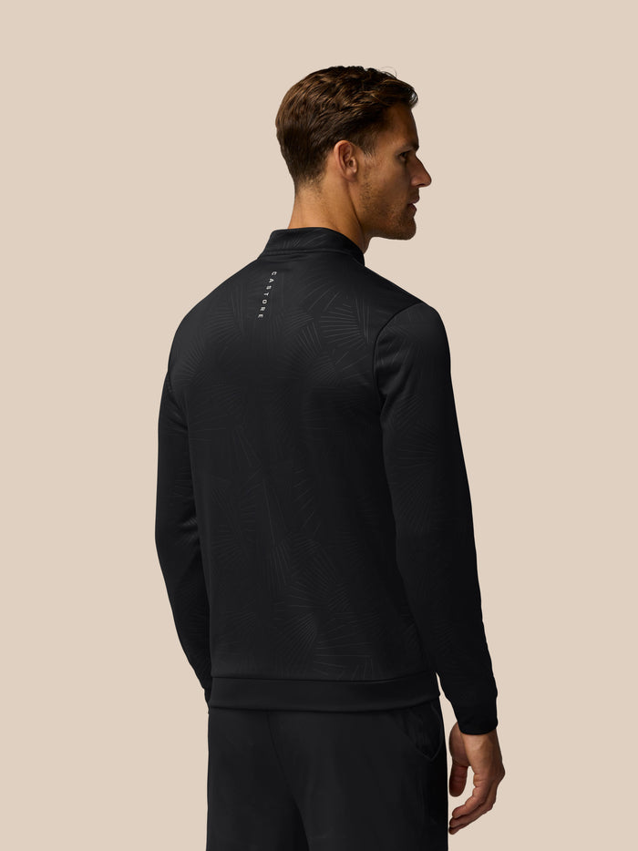 Back view of man wearing black all over print golf top with debossed texture and Castore branding on back and left chest