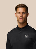 Front view of man wearing black quarter zip golf top with all over pattern and white wing Castore logo on chest