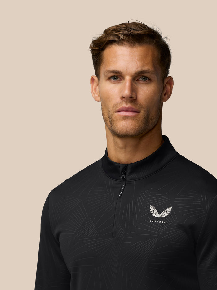 Front view of man wearing black quarter zip golf top with all over pattern and white wing Castore logo on chest