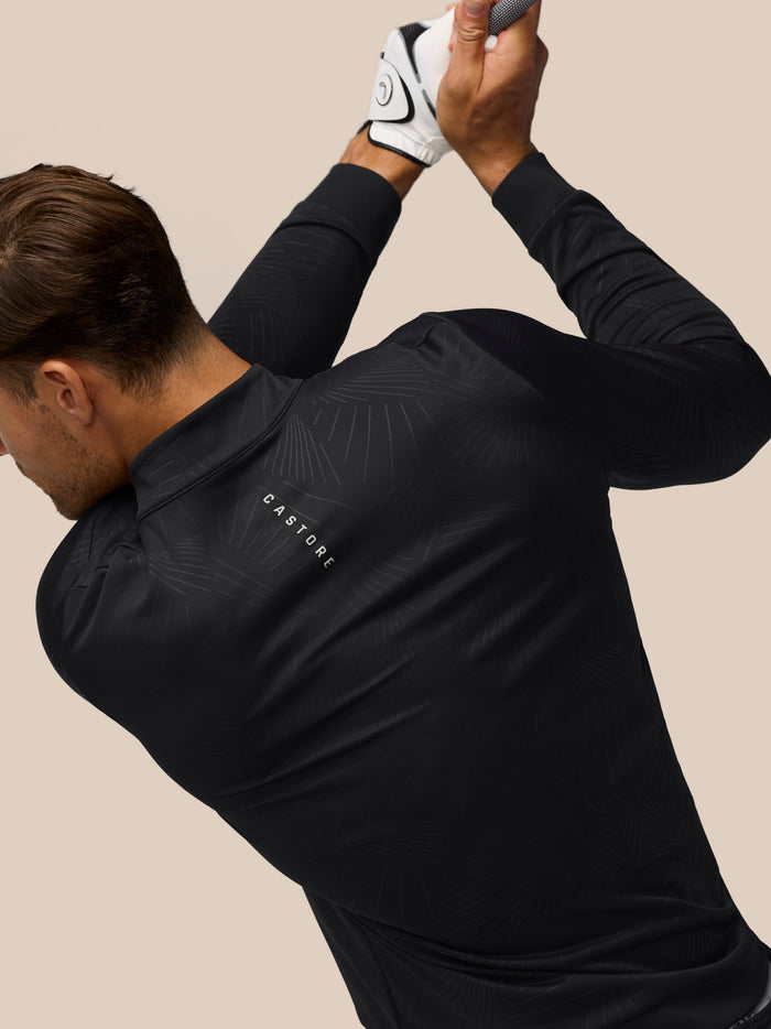 Back and left chest view of man wearing black all over print golf top with subtle pattern and Castore branding
