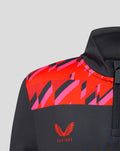 Close-up of Welsh Fire junior performance quarter-zip top showing bold red and pink geometric shoulder panels on dark fabric with Castore branding.
