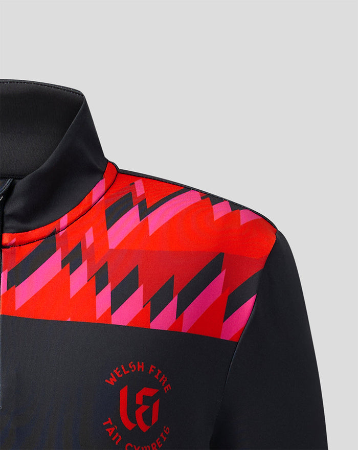Shoulder close-up of the Welsh Fire 2026 junior performance top featuring a bright red geometric shoulder panel against dark fabric.