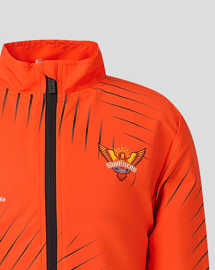 Bright orange Juniors Sunrisers Leeds woven pre match jacket with a black center zipper and diagonal dark stripes.