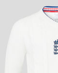 White knitted sweater featuring embroidered crest near the hem and blue trim along the bottom edge.