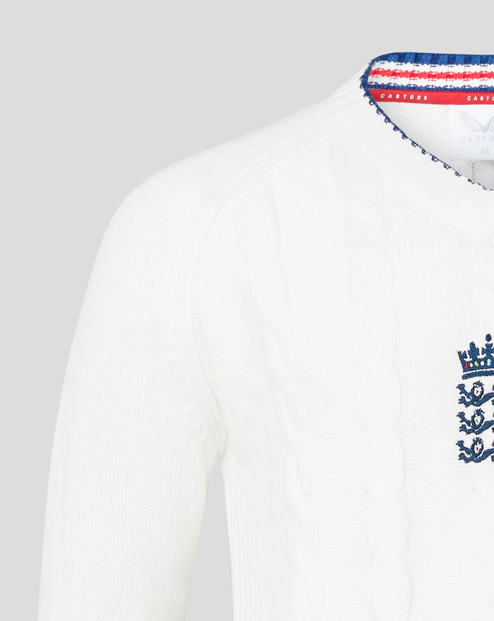 White knitted sweater featuring embroidered crest near the hem and blue trim along the bottom edge.