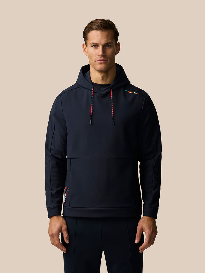 Front view of a model wearing the navy Ashes Travel hoodie with red drawcords and shoulder stripe detail