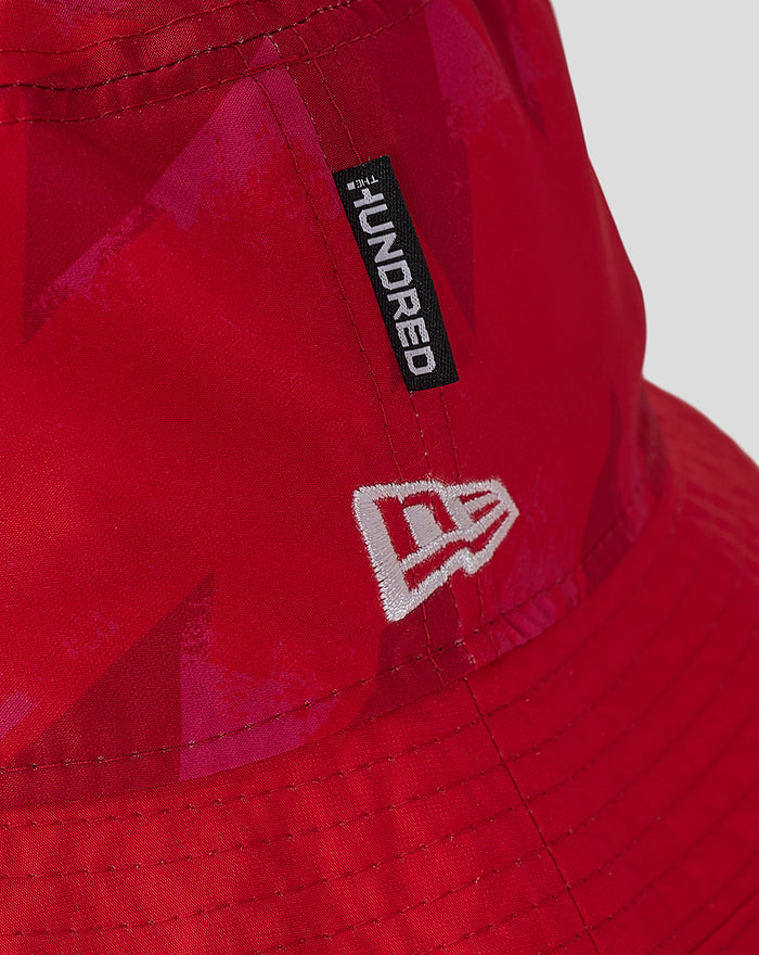Close up on red New Era bucket hat highlighting a black label reading NEW ERA and a white embroidered logo on the side.